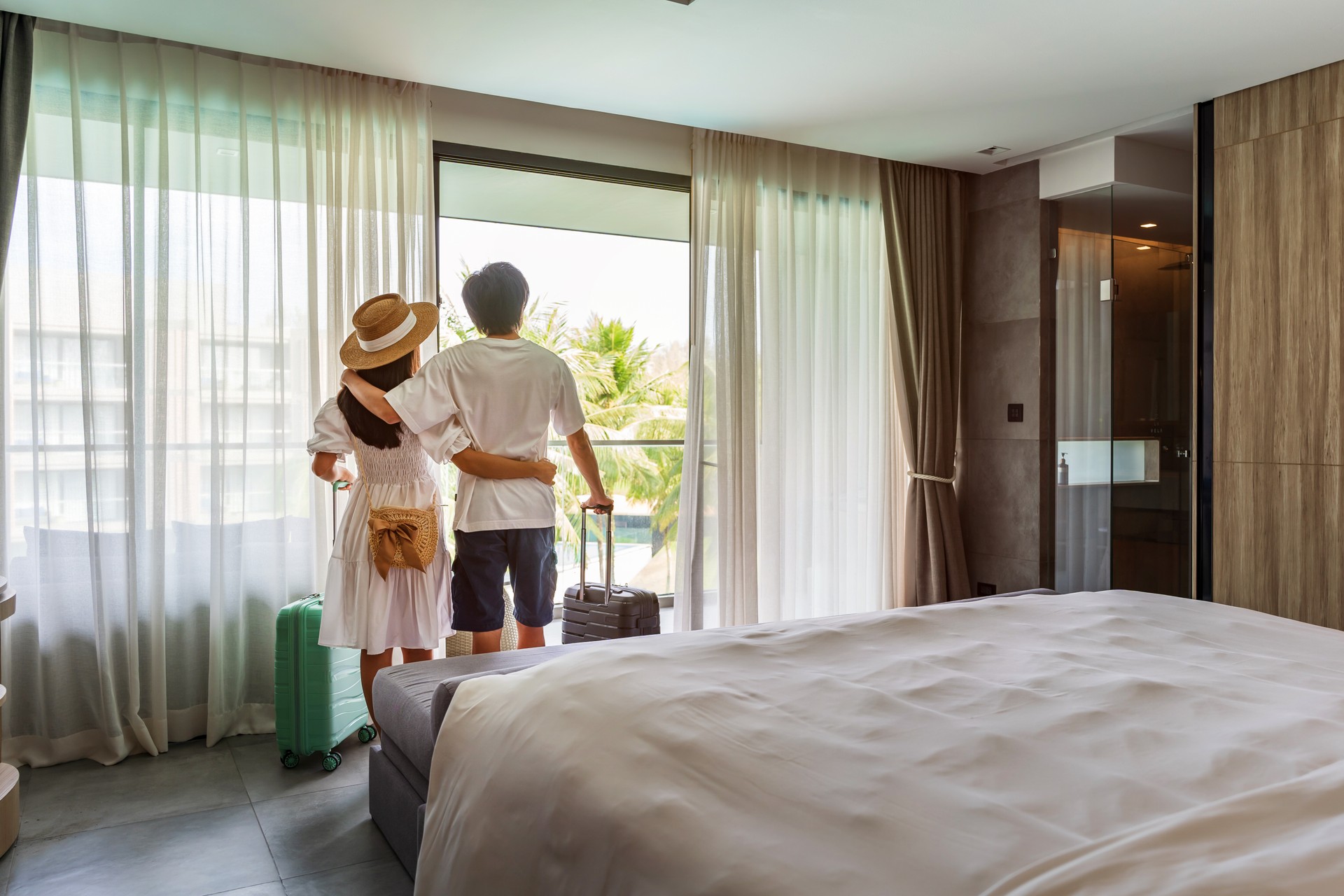 Jovem casal viajante abrindo as cortinas e olhando para a vista da janela de um quarto de hotel durante as férias de verão, conceito de estilo de vida de viagem